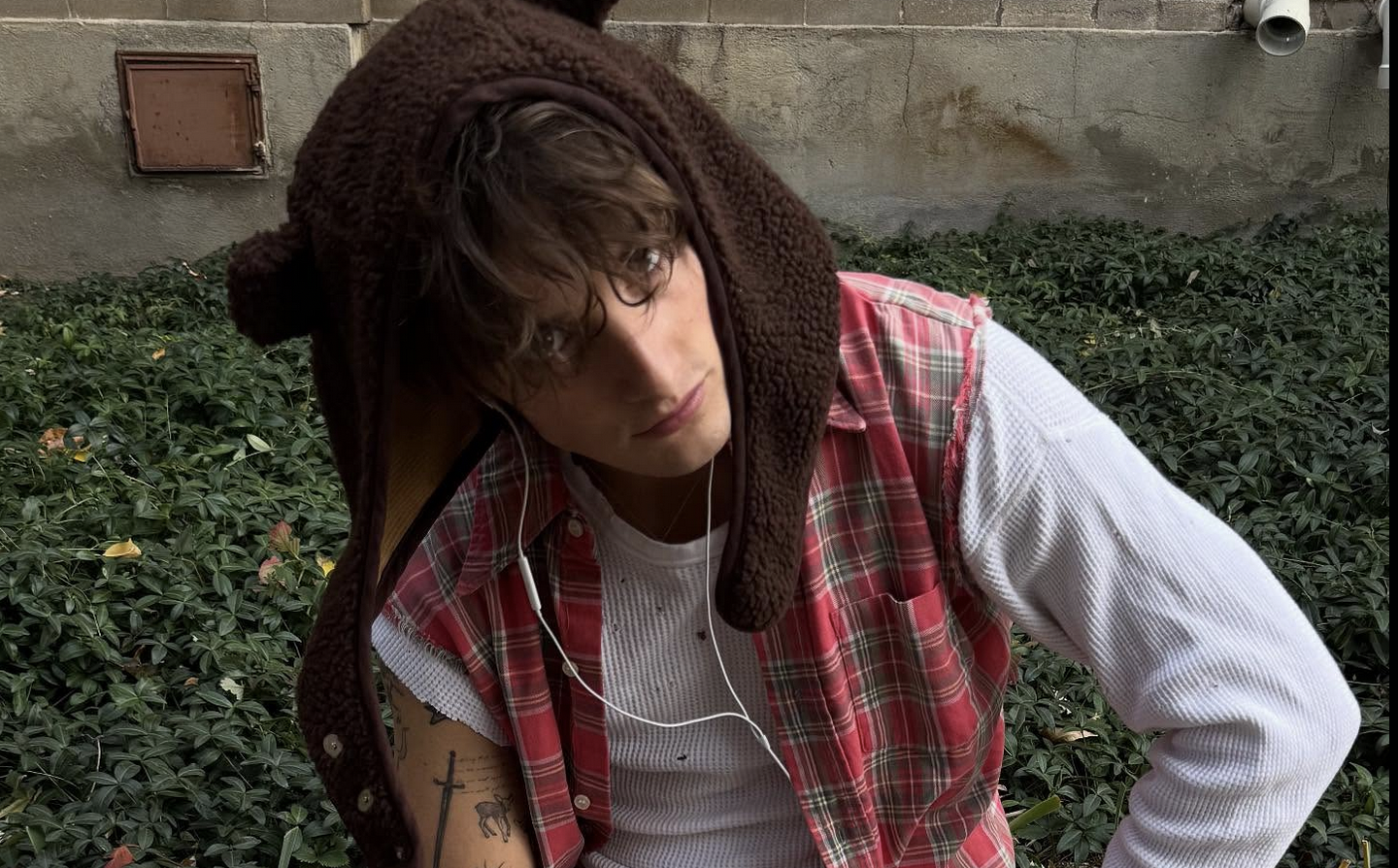 Thomas day looking down at the floor while wearing a flannel and a brown hoodie.